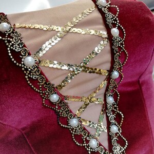 May include: Burgundy velvet bodice with a gold sequin and black lace overlay. The bodice is decorated with white pearl accents.