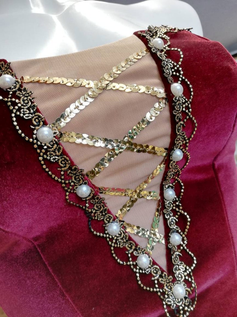 May include: Burgundy velvet bodice with a gold sequin and black lace overlay. The bodice is decorated with white pearl accents.