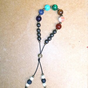 Pode incluir: Um bracelete de contas pretas com uma variedade de contas de pedras preciosas coloridas, incluindo turquesa, verde, marrom, laranja e vermelho. O bracelete tem um cord&atilde;o preto com um fecho de metal e duas contas brancas e pretas na ponta.