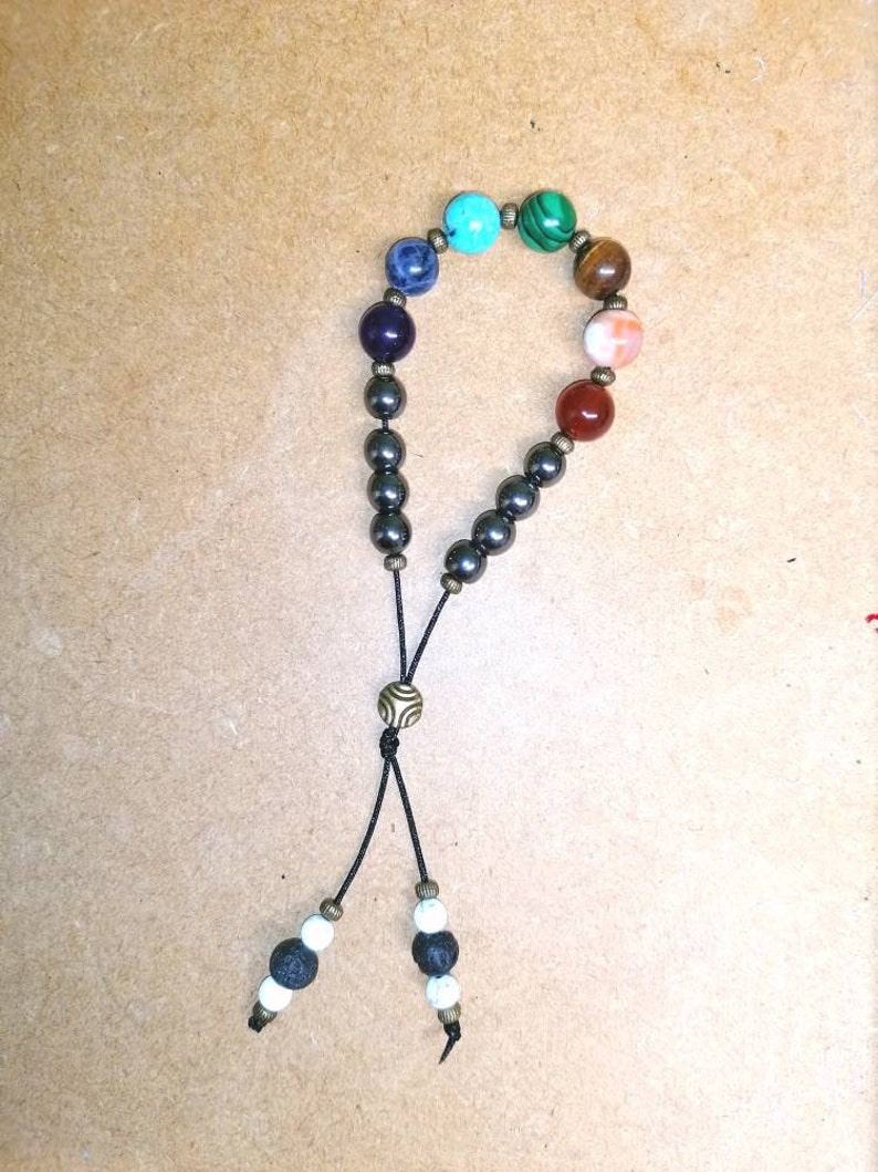 Pode incluir: Um bracelete de contas pretas com uma variedade de contas de pedras preciosas coloridas, incluindo turquesa, verde, marrom, laranja e vermelho. O bracelete tem um cord&atilde;o preto com um fecho de metal e duas contas brancas e pretas na ponta.