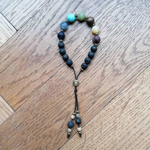 Pode incluir: Um bracelete com contas de v&aacute;rias cores e contas de lava preta. O bracelete tem uma borla com um fecho de metal na ponta.