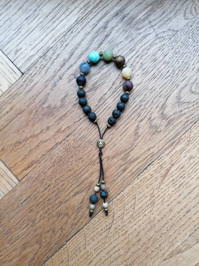 Pode incluir: Um bracelete com contas de v&aacute;rias cores e contas de lava preta. O bracelete tem uma borla com um fecho de metal na ponta.