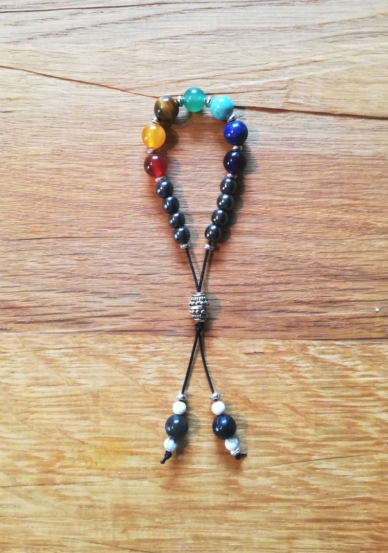 Pode incluir: Um bracelete de contas pretas com um arco-&iacute;ris de pedras coloridas, incluindo verde, azul, amarelo, laranja e vermelho. O bracelete tem uma conta prateada e um cord&atilde;o preto com contas brancas na ponta.