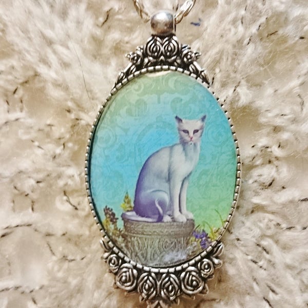 Collier pendentif chat Siamois aux yeux bleu assis sur une margelle de puit, chat blanc sur fond en Camaïeu de vert et de bleu