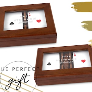 May include: Two wooden boxes with clear tops, each containing playing cards and dice. The cards show a club, an ace of hearts, and an ace of spades. The text "Stephanie Bridesmaid" is visible on the cards. The boxes are on a white background.