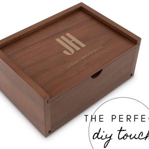 Peut inclure: Une boîte rectangulaire en bois brun chaud avec un couvercle coulissant. Le couvercle porte les initiales "JH" et l'inscription "JASON - GROOMSMAN". La boîte a une petite ouverture circulaire. Une touche DIY.