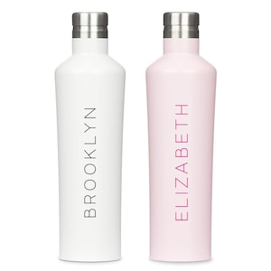 K&ouml;nnte beinhalten: Zwei hohe, zylindrische Wasserflaschen mit metallisch silbernen Schraubverschl&uuml;ssen. Die linke Flasche ist mattwei&szlig; und tr&auml;gt den Namen BROOKLYN in schwarzer vertikaler Schrift. Die rechte Flasche ist matt hellrosa mit dem Namen ELIZABETH.