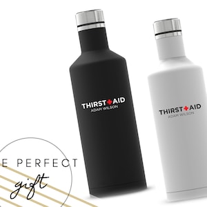 Puede incluir: Dos botellas de agua de acero inoxidable con una cruz blanca y las palabras "THIRST+AID" y "ADAM WILSON" en ellas. Las botellas son negras y blancas. El texto "THE PERFECT gift" est&aacute; en la esquina inferior izquierda de la imagen.