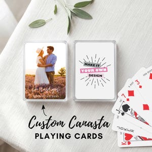 May include: Custom Canasta playing cards with a photo of a couple in a field on one side and the text "Make it your own design" on the other. The cards are in a clear plastic case. A few playing cards are fanned out.
