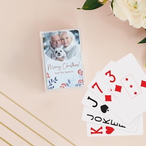 May include: A deck of playing cards with a clear plastic case featuring a photo of a smiling couple and a small white dog. The text "Merry Christmas! love the tanners" is printed on the case. Several playing cards are fanned out.