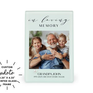 May include: A rectangular printed glass frame with a family photo. The frame is light green with the words "in loving memory" at the top. The photo features a man and two children. The frame is 10.8 cm x 15.9 cm.
