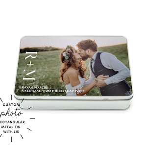 May include: Rectangular metal tin with lid featuring a custom photo of a couple kissing in a field. The tin has the text "R+M" and "RAYA & MARCUS A KEEPSAKE FROM THE BEST DAY EVER!" printed on it. The words "CUSTOM photo RECTANGULAR METAL TIN WITH LID" are also printed on the tin.