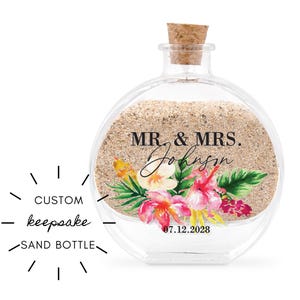 Pode incluir: Uma garrafa de areia redonda de vidro transparente com rolha de cortiça. A garrafa é preenchida com areia e decorada com arte floral e o texto "MR. & MRS. Johnson" e uma data. A garrafa é rotulada "CUSTOM keepsake SAND BOTTLE."