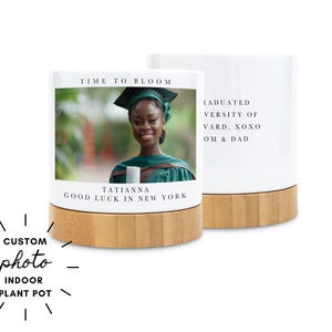 May include: White indoor plant pot with a bamboo base. The front displays a photo of a graduate with the text "TIME TO BLOOM" and "TATIANNA GOOD LUCK IN NEW YORK". The back has text that reads "GRADUATED UNIVERSITY OF VARD, XOXO OM & DAD".