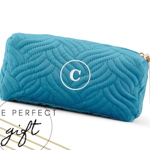 Könnte beinhalten: Türkisfarbene, gesteppte Kosmetiktasche mit Zickzackmuster und einem weißen Monogramm "C" in einem Kreis. Die Tasche hat einen goldenen Reißverschluss mit einer cremefarbenen Quaste. Der Text "THE PERFECT gift" ist ebenfalls sichtbar.