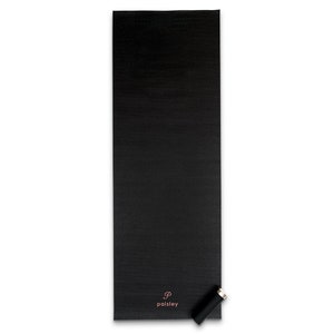 May include: A rectangular black yoga mat with a smooth, matte texture. Near the bottom right corner, the letter P is printed in a rose gold script font above the word paisley in a matching rose gold sans-serif font. A small black cylinder.