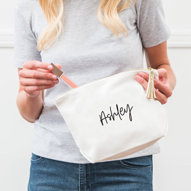 May include: White canvas zippered pouch with a gold tassel and the name "Ashley" written in black script.