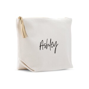 May include: A white canvas zippered pouch with a gold tassel and the name "Ashley" written in black cursive.