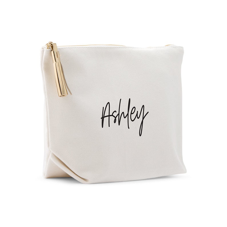 May include: A white canvas zippered pouch with a gold tassel and the name "Ashley" written in black cursive.