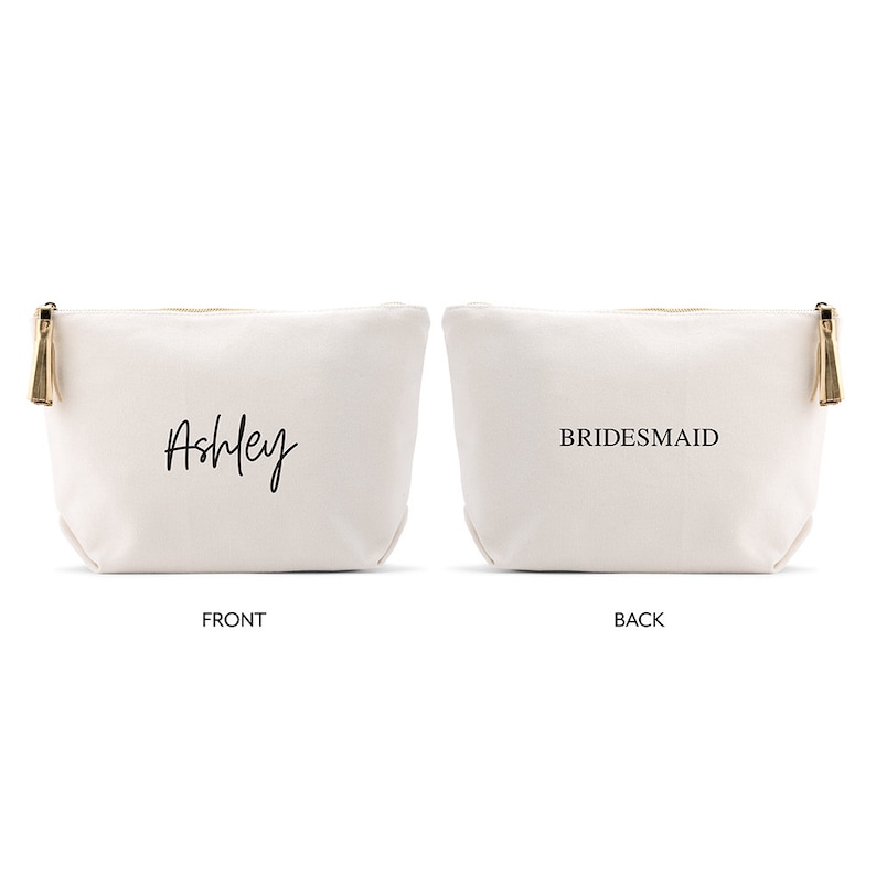 May include: A white canvas makeup bag with a gold zipper and tassel. The front of the bag says "Ashley" in black script. The back of the bag says "BRIDESMAID" in black.