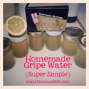Może przedstawiać: Zbliżenie na pięć szklanych słoików wypełnionych jasnożółtym płynem, z etykietą "Homemade Gripe Water (Super Simple)" i "www.MommaBish.com". W tle widoczne jest pudełko z organiczną herbatą z rumianku.