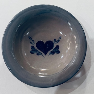 May include: A gray ceramic bowl with a blue heart and leaf design. The bowl is glazed and has a slight sheen.