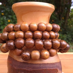 May include: A wooden bracelet with multiple strands of brown beads. The bracelet is wrapped around a wooden vase.