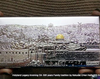 May include: A silver metal box with a detailed image of the city of Jerusalem. The box has a gold dome on top and the word "Jerusalem" printed on the bottom. The text "Holyland Legacy Anointing Oil - 500 years Family tradition by Nekudat Chen Haifa 972-546818597" is printed below the box.