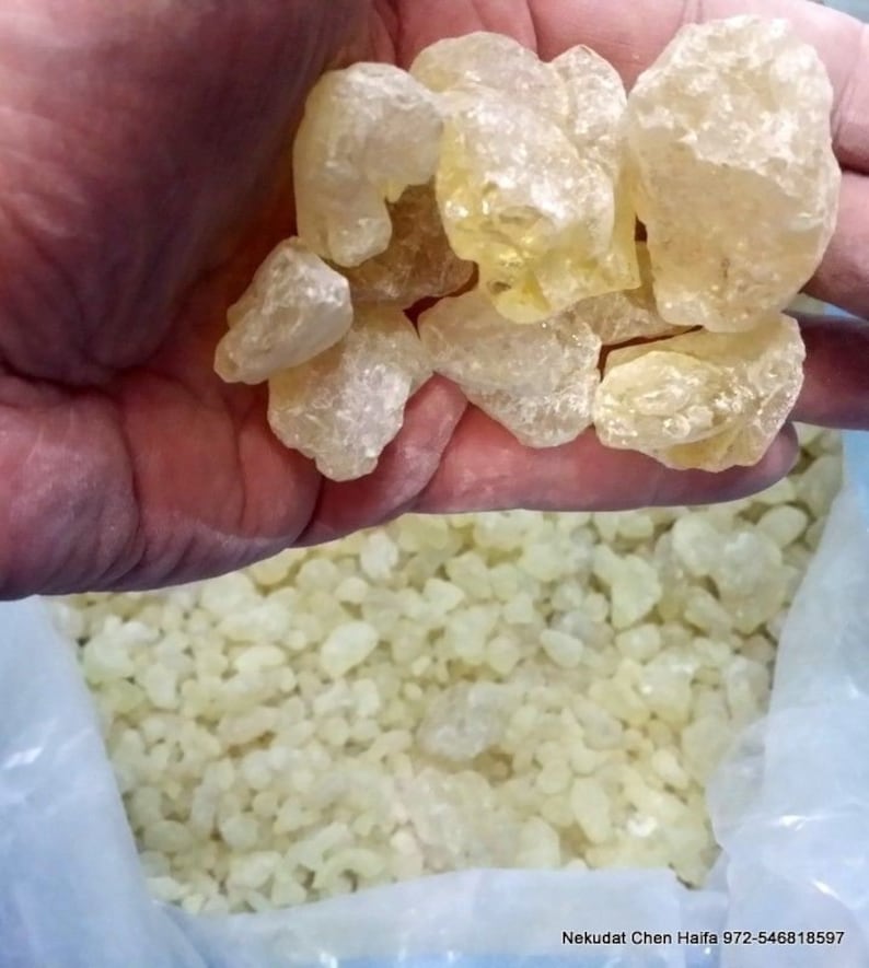 Puede incluir: Primer plano de un pu&ntilde;ado de piezas de resina transl&uacute;cida de color amarillo p&aacute;lido, con una mayor cantidad de la misma resina en una bolsa de pl&aacute;stico en el fondo. La bolsa tiene el texto "Nekudat Chen Haifa 972-546818597" impreso en ella.