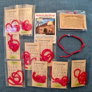 Peut inclure: Une collection de bracelets en fil rouge avec des perles œil bleu, emballés avec des cartes présentant la prière Ben Porat en anglais et en hébreu, ainsi qu'une carte intitulée Kabbalah Red Strings against evil eye et une carte Prayer for Traveler.