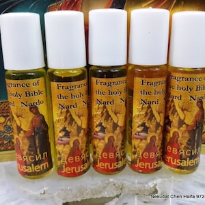 May include: Five small, clear glass bottles with white roll-on tops. Each bottle contains a yellow liquid and has a label with a religious image and the text "Fragrance of the holy Bible Nard" in English. The labels also have text in a foreign language.