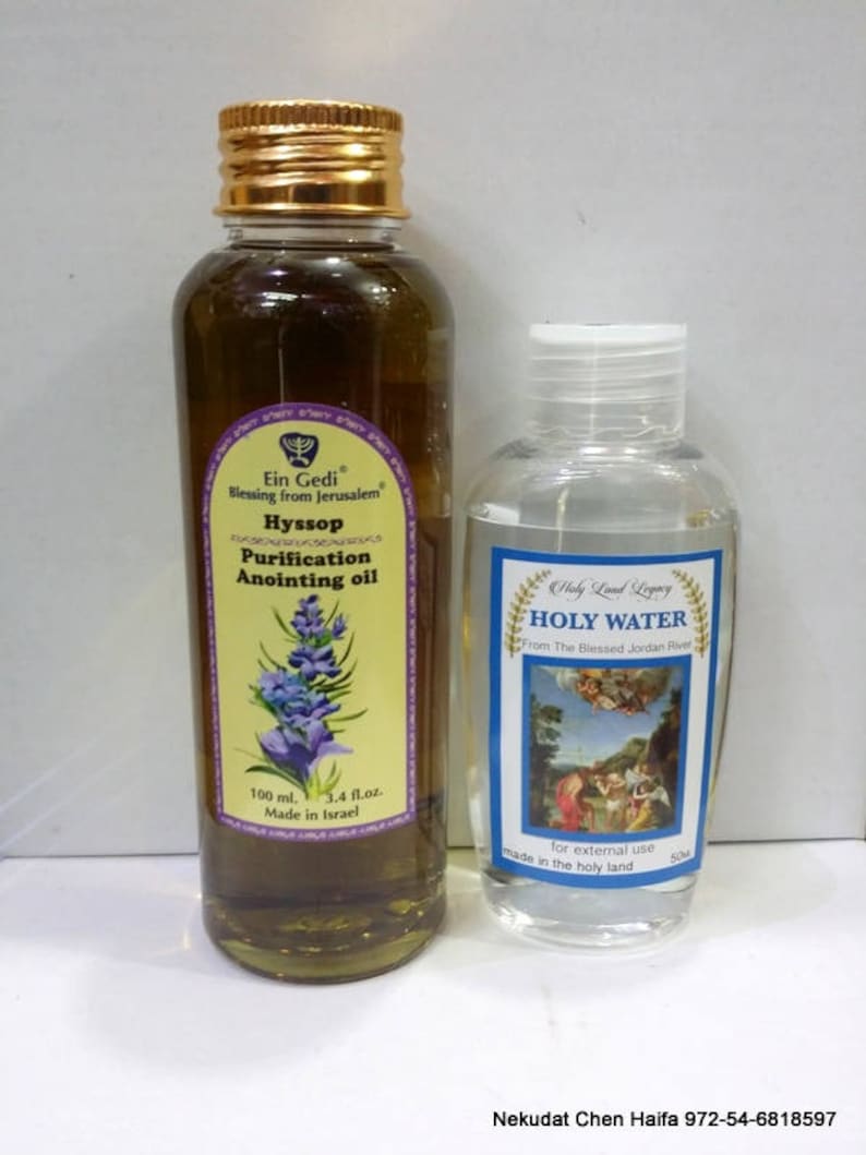 May include: Two glass bottles with gold lids. The bottle on the left is green and contains Hyssop Purification Anointing Oil, made in Israel. The bottle on the right is clear and contains Holy Water from the Blessed Jordan River, made in the Holy Land. The bottles are on a white surface.