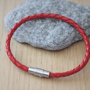 May include: A red leather bracelet with a braided design and a silver magnetic clasp.