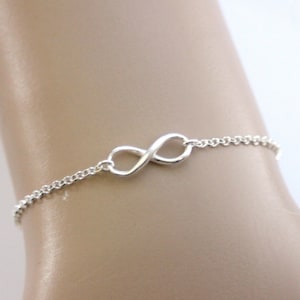 Op de afbeelding: Een zilveren armband met een oneindigheidssymbool bedel. De armband is gemaakt van een delicate ketting en heeft een eenvoudige oneindigheidssymbool bedel.
