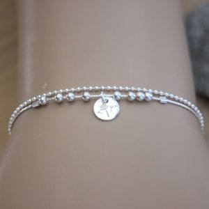 May include: A silver bracelet with a delicate chain and small beads. A charm with a tree design hangs from the center of the bracelet.