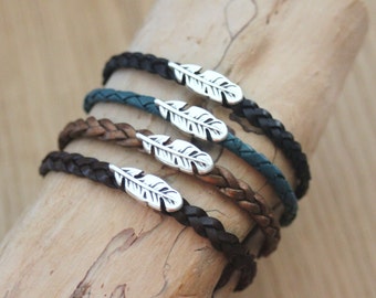 Pulsera unisex de piel trenzada con dije de pluma de metal, disponible en 4 colores de piel.