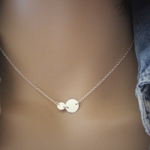 May include: A silver necklace with two round pendants. The larger pendant is on the right and the smaller pendant is on the left.