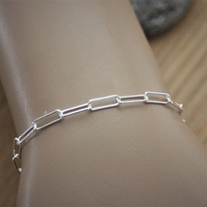 May include: A silver chain bracelet with a simple, rectangular link design.