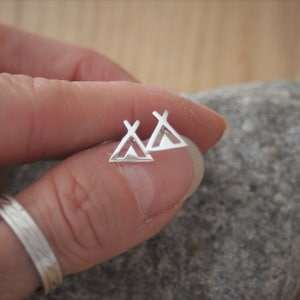 May include: A pair of silver tent-shaped stud earrings. The earrings are small and delicate, and they are perfect for adding a touch of whimsy to any outfit.
