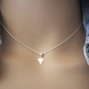 May include: A silver chain necklace with a small triangle pendant.