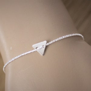 Peut inclure: Un bracelet en argent délicat avec une chaîne scintillante et un charm triangulaire. Le charm porte l'inscription "one". Le bracelet est un bijou simple et élégant.