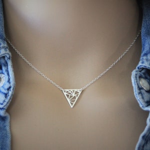 Op de afbeelding: Een zilveren ketting met een geometrische driehoekige hanger. De hanger is gemaakt van een delicaat, opengewerkt ontwerp.