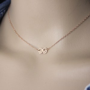 Op de afbeelding: Een delicate roségouden ketting met een hanger in de vorm van een pootafdruk. De ketting wordt getoond op de hals van een persoon, met een spijkerjasje op de achtergrond. De ketting is fijn en de hanger is klein.
