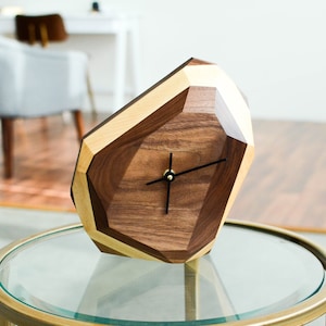 May include: A geometric wooden clock with a walnut and maple wood design. The clock has black hands and a gold center.