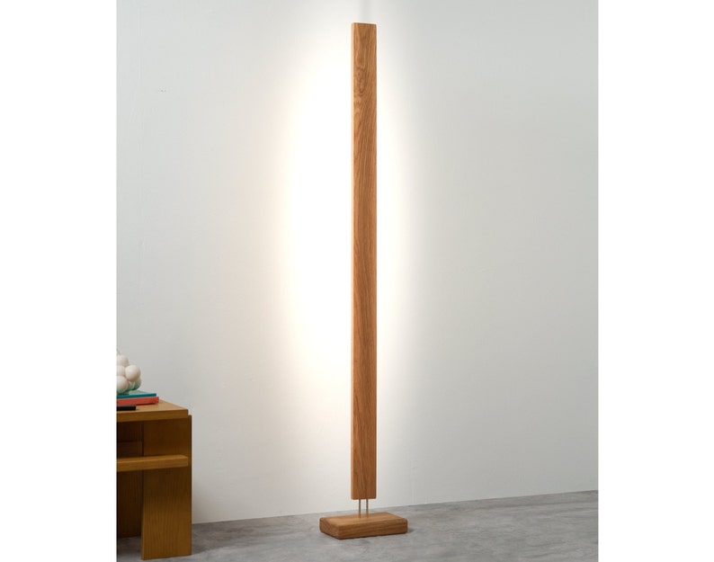 May include: A tall, wooden floor lamp with a rectangular design. The lamp has a warm, natural wood finish and a bright, vertical light strip. The base is a matching wooden block. The lamp is approximately 72 inches tall.