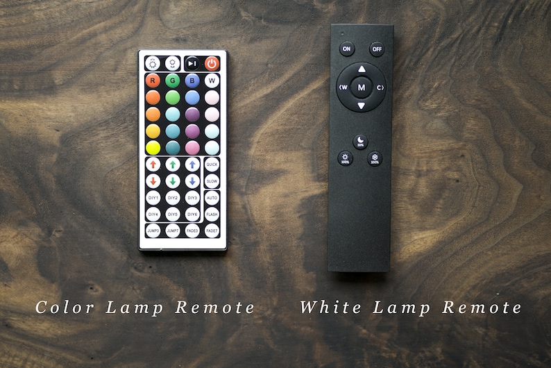 May include: Two lamp remotes on a wooden surface. One is white with colored buttons and the text "Color Lamp Remote". The other is black with function buttons and the text "White Lamp Remote".