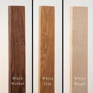 May include: Three wooden planks in a vertical arrangement, each with a different wood type. From left to right, the planks are black walnut, white oak, and white maple. Each plank has the wood type labeled in white text.