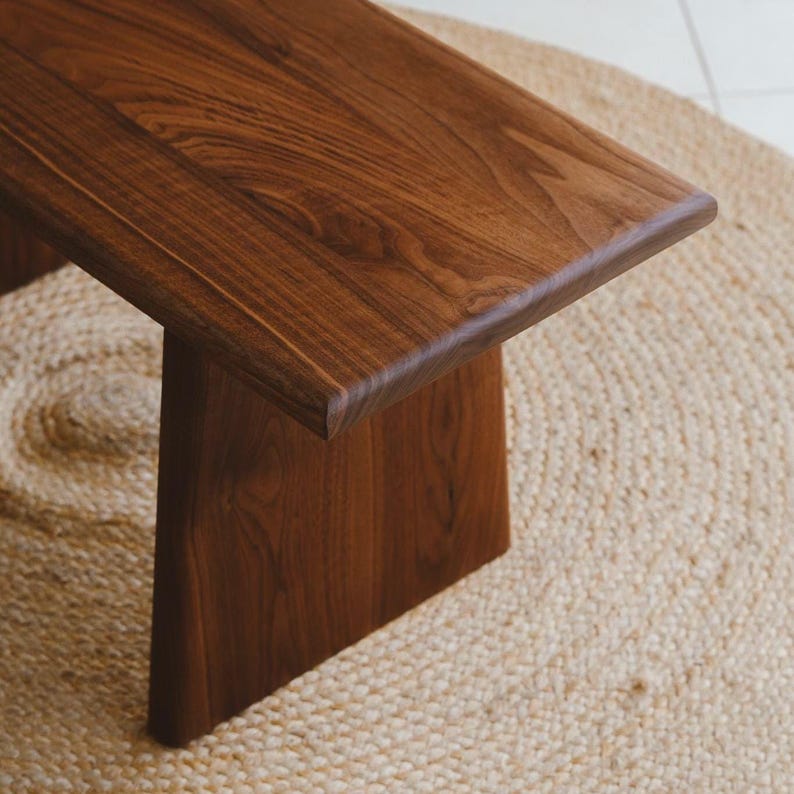 Puede incluir: Un banco de madera con una superficie lisa de color marr&oacute;n oscuro y un patr&oacute;n de veta natural visible. El banco est&aacute; construido con una parte superior rectangular plana y una pata de soporte s&oacute;lida e inclinada que se extiende hacia abajo.