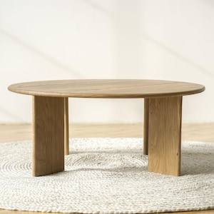 May include: A round, light-coloured wooden coffee table with a natural finish. The table has a simple design with a circular top and four rectangular legs. The table is approximately 91 cm in diameter.