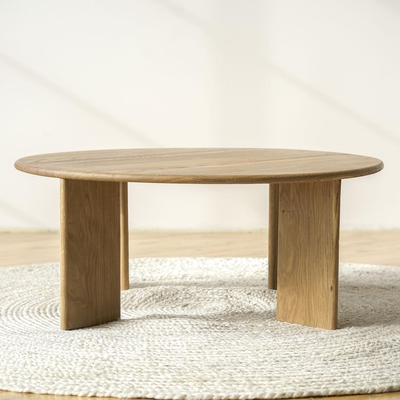May include: A round, light-coloured wooden coffee table with a natural finish. The table has a simple design with a circular top and four rectangular legs. The table is approximately 91 cm in diameter.